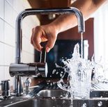 En person som overfyller et glass med vann i en moderne kjøkkenvask av rustfritt stål