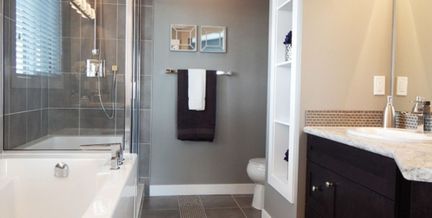 Et moderne bad med en mørk vask og lys benkeplate, et hvitt badekar og en dusj med glass dører og vegger hvor mye naturlig lys slipper inn gjennom persiennene fra vinduet over badekaret