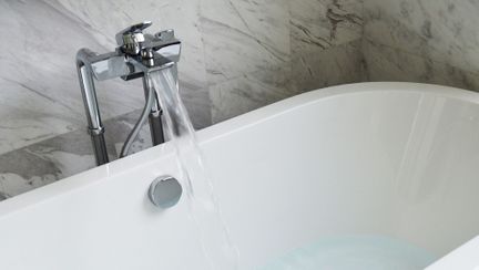Et hvitt og moderne badekar som fylles opp med vann av en stål kran med godt trykk